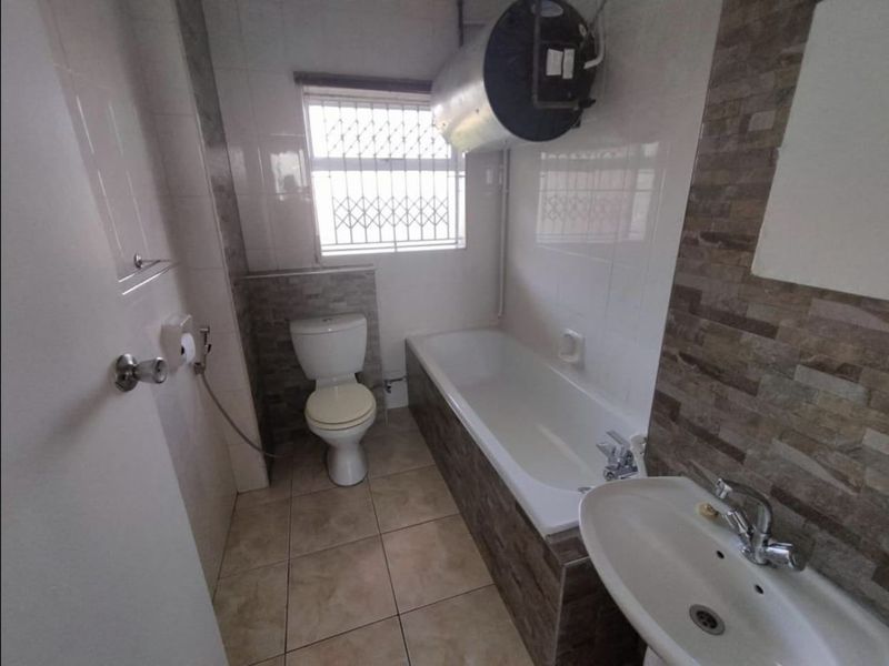 A functional bathroom featuring a bathtub, pedestal basin, toilet, and an exposed wall-mounted water heater.