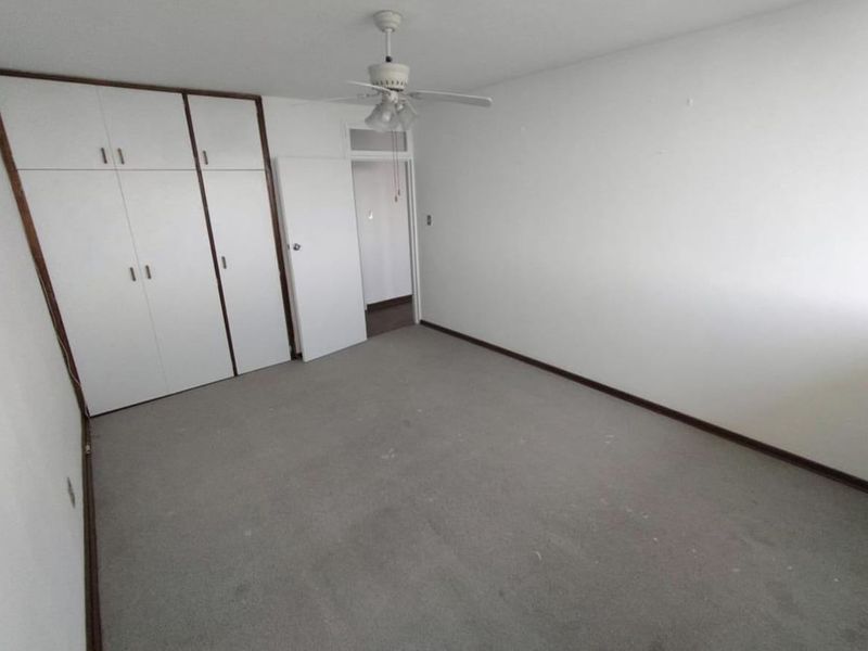 A vacant bedroom featuring built-in cupboards, a ceiling fan, and neutral carpeting, offering a blank canvas for personalization.