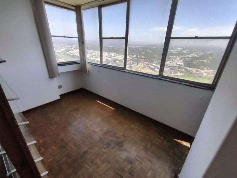 A bright, empty room featuring classic parquet flooring and expansive windows offering panoramic city and landscape views.
