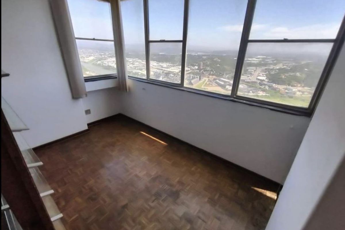 A bright, empty room featuring classic parquet flooring and expansive windows offering panoramic city and landscape views.