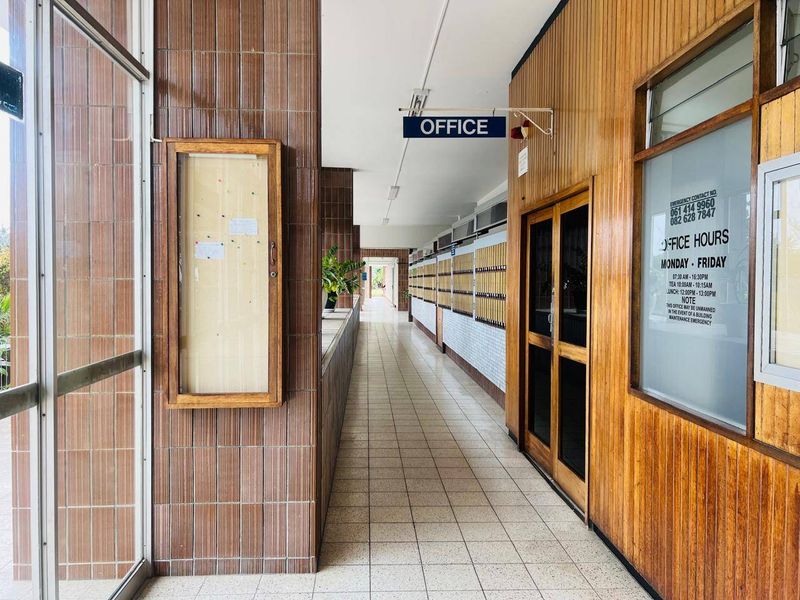 A communal hallway featuring tiled flooring, wood-paneled walls, and a series of built-in mailboxes, leading towards an office area.