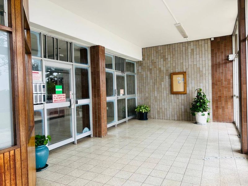 A bright and spacious apartment building entrance lobby featuring tiled flooring, glass panel doors, and decorative brick-style wall cladding.