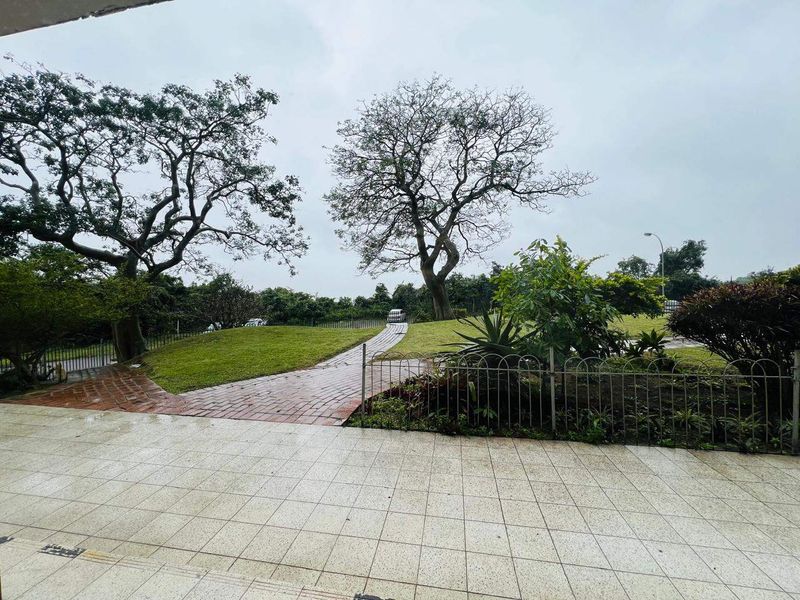 A view of a paved patio area leading out to a landscaped garden with mature trees and a brick pathway.