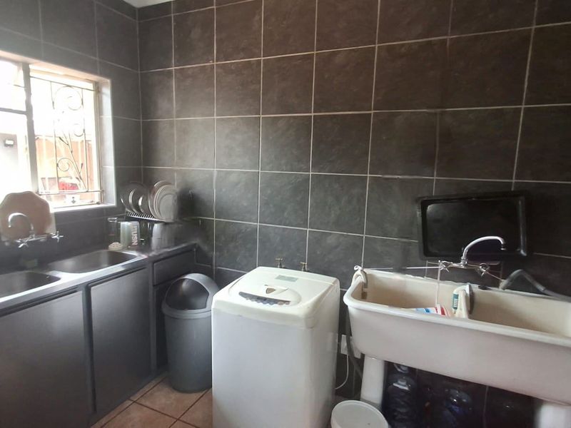 A functional laundry room featuring a stainless steel sink, a utility trough, and dark ceramic wall tiling.