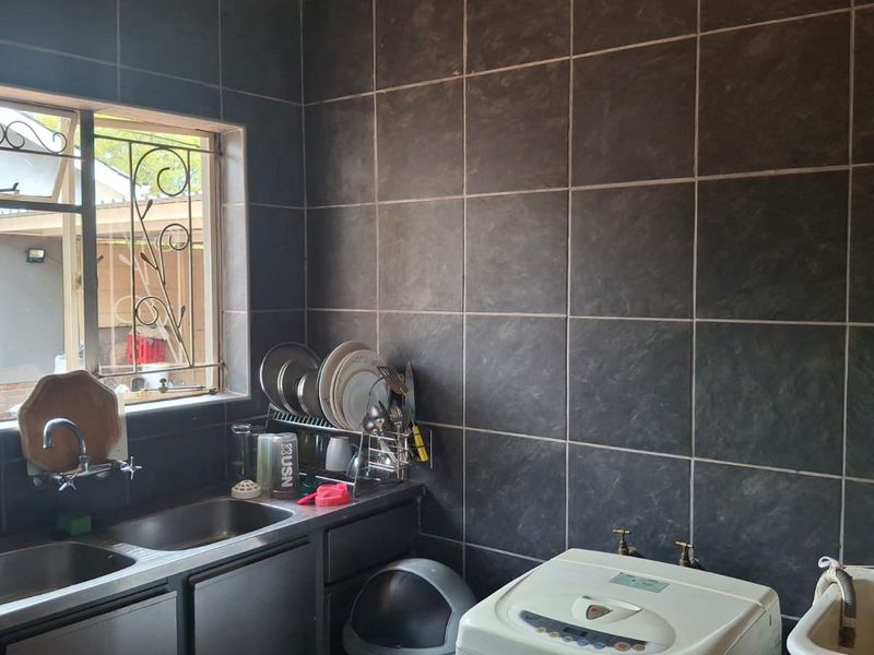 A functional laundry area featuring dark tiled walls, a double stainless steel sink, and dedicated plumbing connections for laundry appliances.