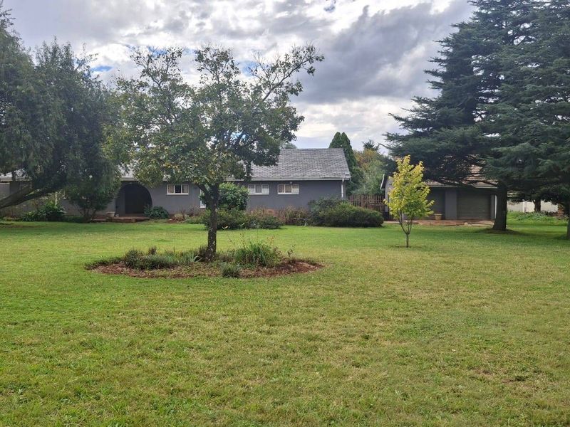 A view of the rear of the house featuring a large, well-maintained lawn, mature trees, and a detached garage.