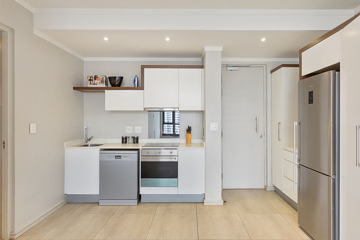 Modern compact kitchen featuring white cabinetry, stone countertops, integrated dishwasher, stainless steel oven, and hob, complemented by neutral tiled flooring and recessed lighting.