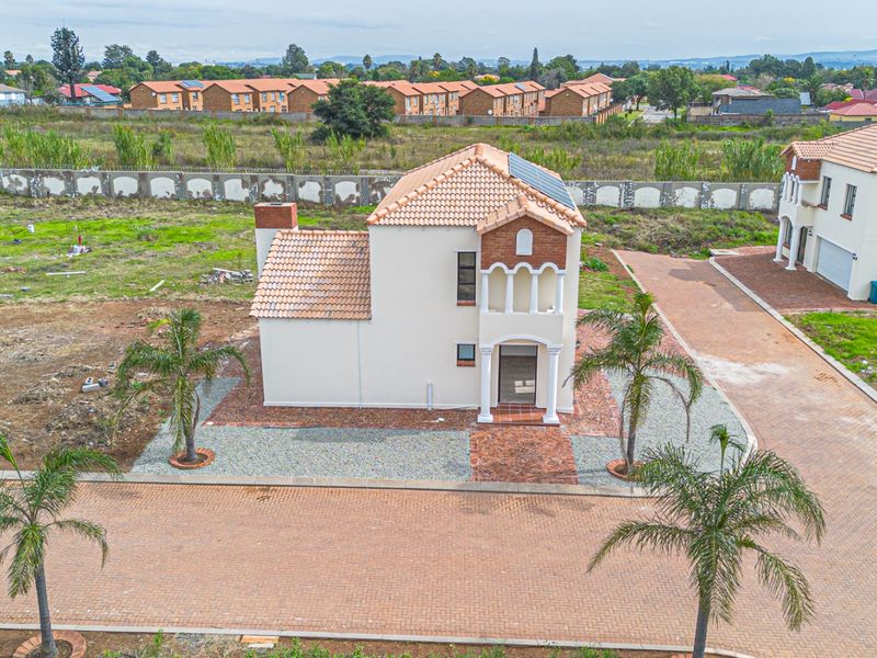 Aerial view of a detached two-story house featuring a terracotta tiled roof, solar panels, and a brick-paved driveway within a residential estate.