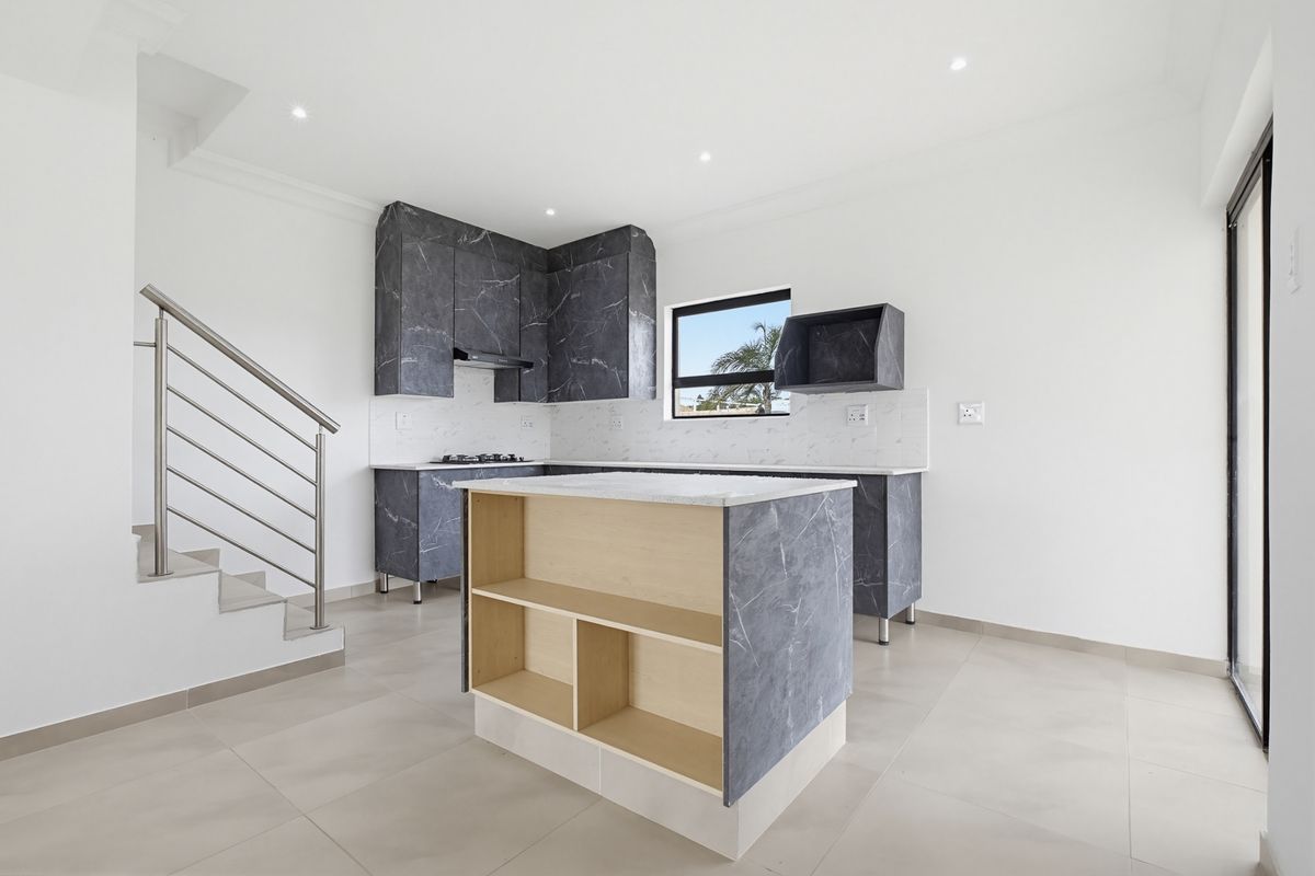 Modern kitchen featuring dark marble-effect cabinetry, a central island, gas hob, and sleek tiled flooring, adjacent to an internal staircase.