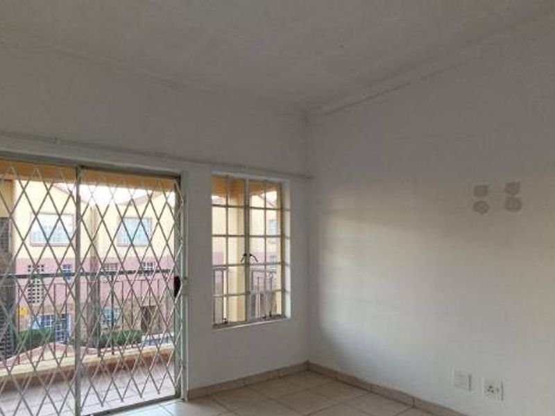 An empty living room featuring tiled flooring, a sliding glass door with a security gate, and windows with burglar bars.