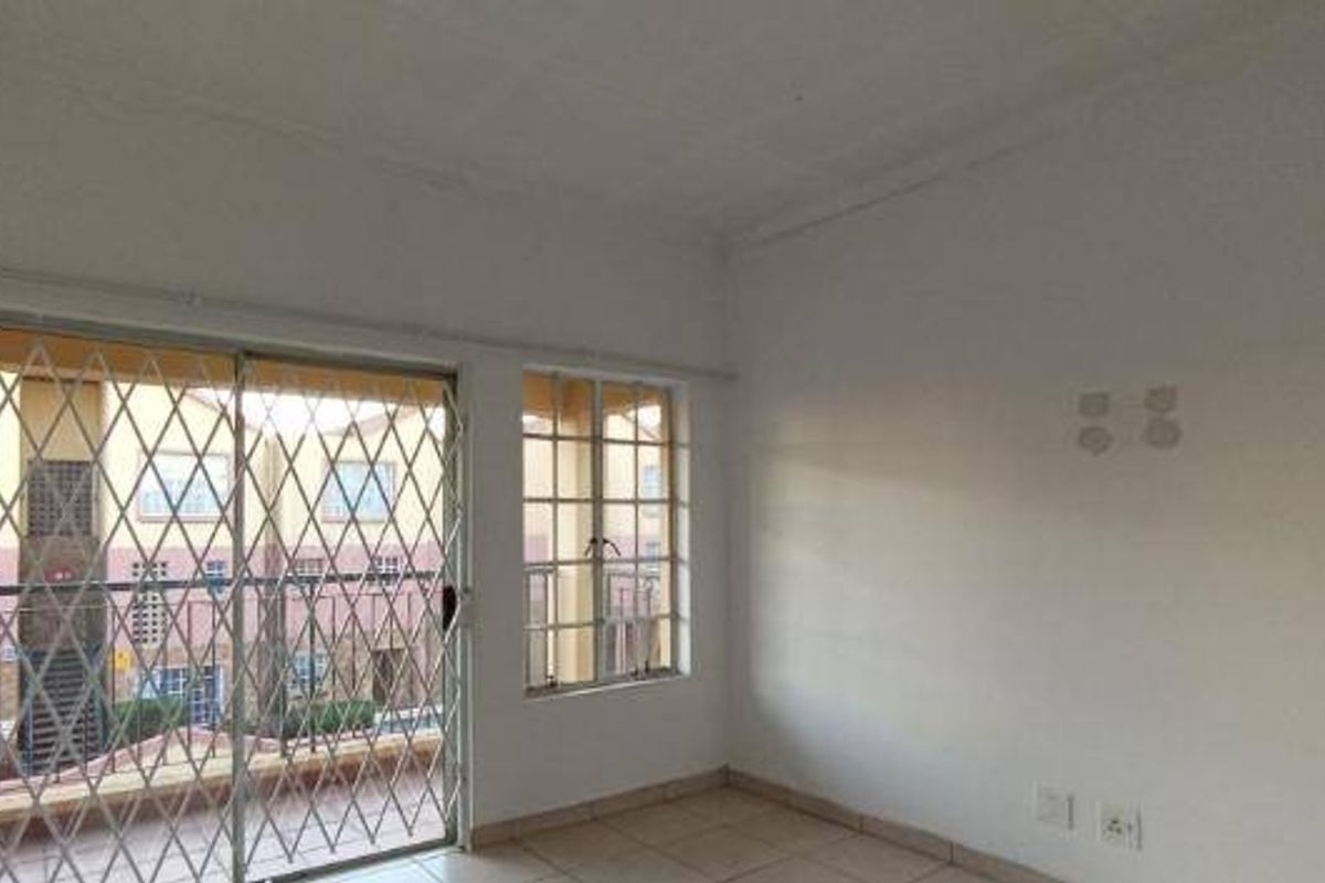 An empty living room featuring tiled flooring, a sliding glass door with a security gate, and windows with burglar bars.