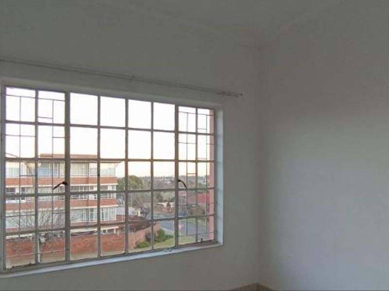 A vacant bedroom featuring a large window with security bars and a curtain rail, offering a view of the surrounding neighborhood.