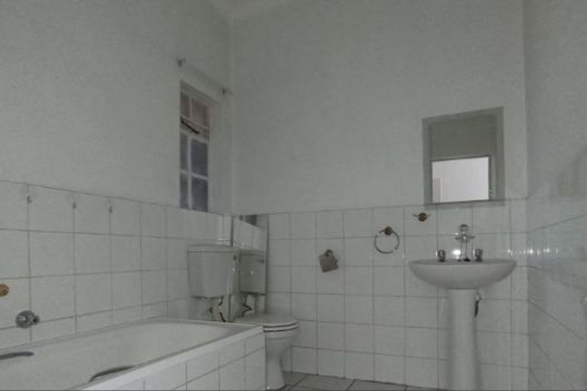A functional bathroom featuring a pedestal basin, bathtub, and toilet with white wall tiling throughout.