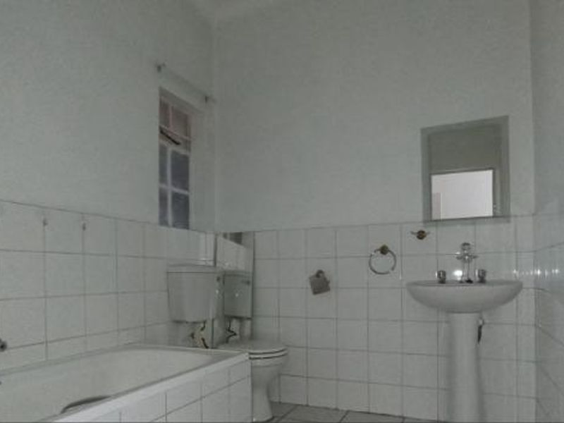 A functional bathroom featuring a pedestal basin, bathtub, and toilet with white wall tiling throughout.