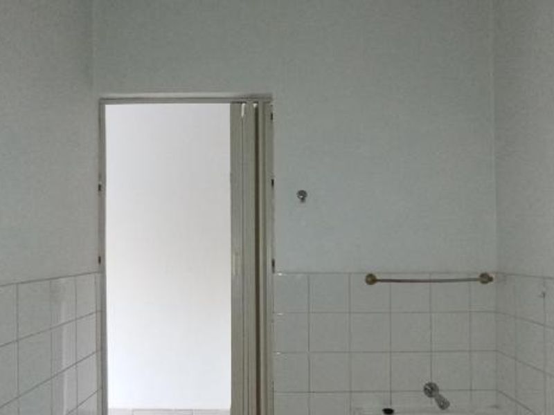 A basic, empty bathroom featuring white wall tiles, a towel rail, and a folding door entrance.