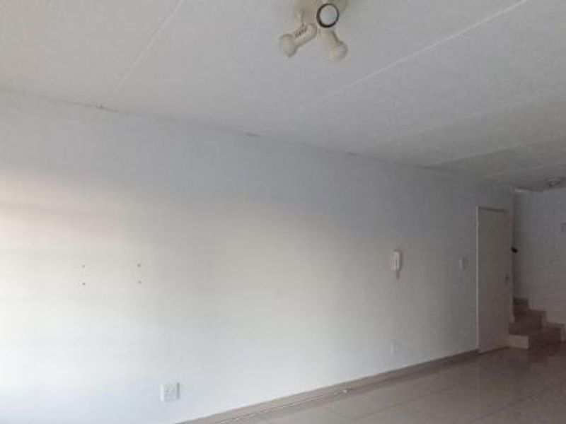 An empty open-plan living and kitchen area featuring tiled flooring, neutral walls, and basic kitchen cabinetry, offering a blank canvas for renovation.
