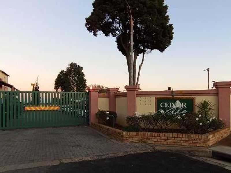 The entrance to Cedar Ville apartment complex featuring a secure gated access point, brick boundary walls, and established landscaping.