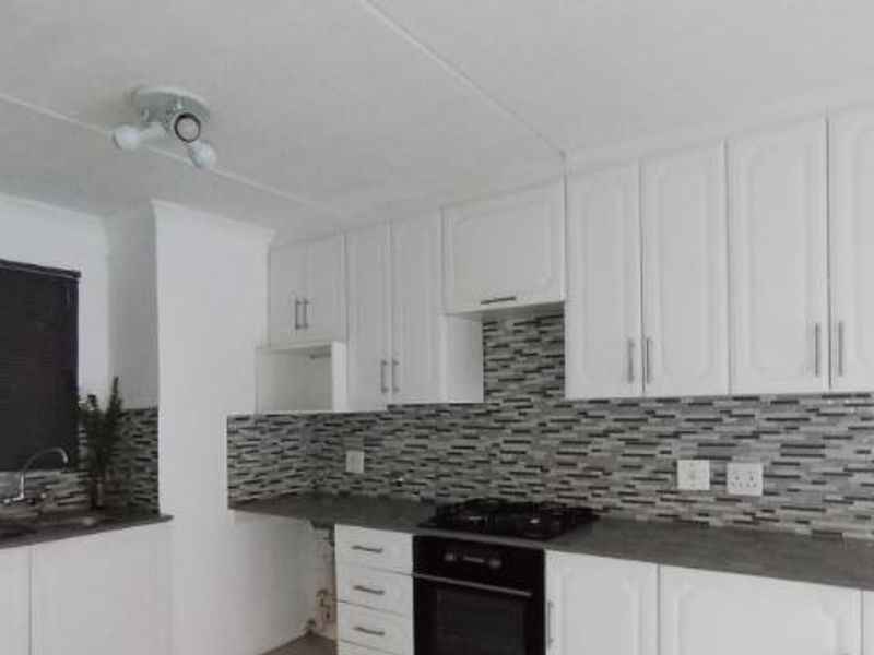A clean, functional kitchen featuring white cabinetry, a modern mosaic tile backsplash, dark laminate countertops, and integrated gas cooking appliances.