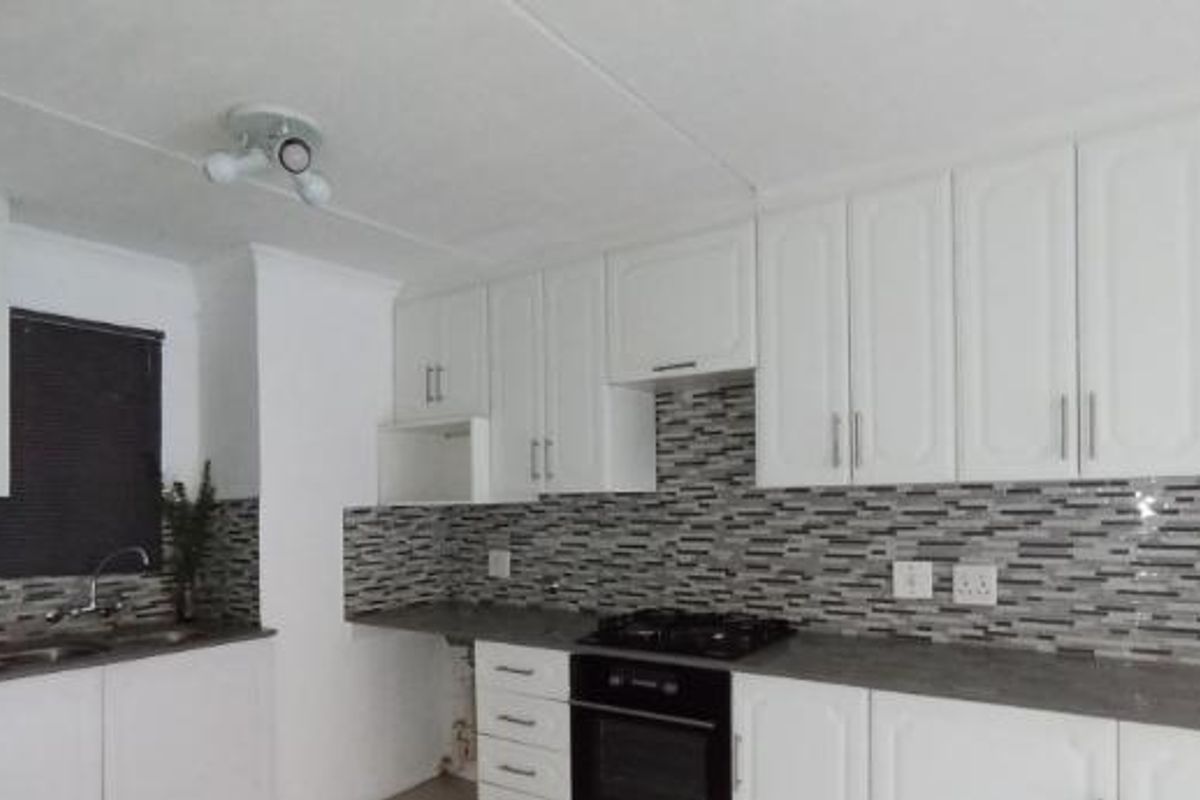 A clean, functional kitchen featuring white cabinetry, a modern mosaic tile backsplash, dark laminate countertops, and integrated gas cooking appliances.