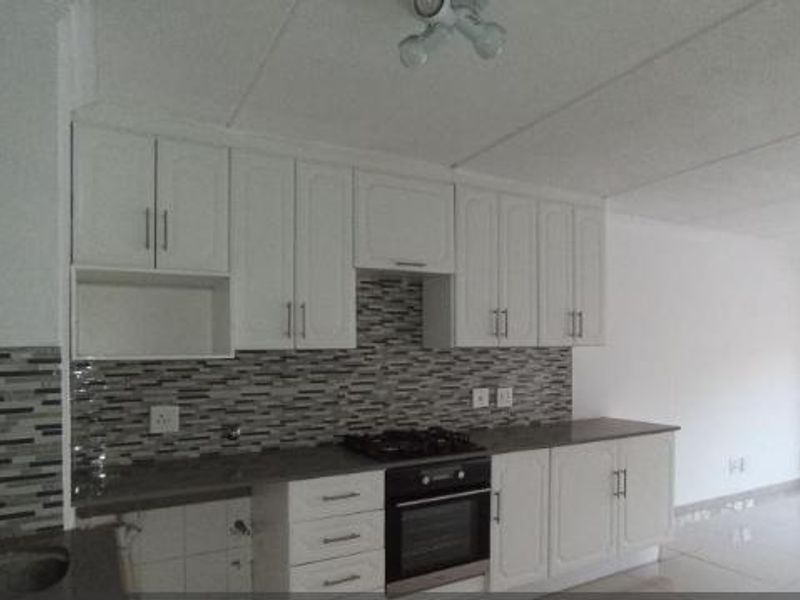 Open-plan kitchen featuring white cabinetry, mosaic tile backsplash, and built-in oven, flowing into a bright living area with access to a balcony.
