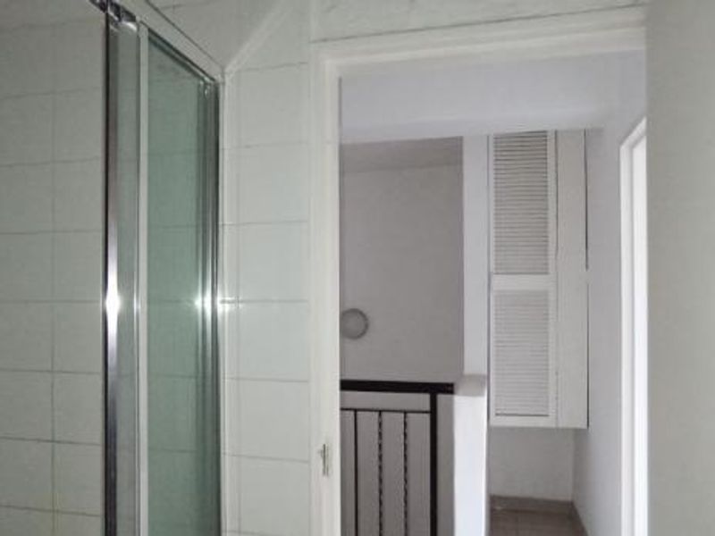 A functional bathroom featuring a glass shower enclosure with tiled walls, leading into an adjacent hallway area with built-in storage cabinetry.