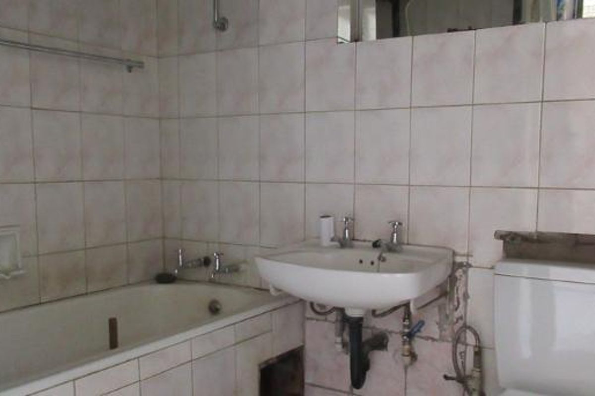 A dated bathroom featuring a bathtub, pedestal basin, and toilet, currently requiring significant maintenance and cosmetic updates to the tiling and plumbing fixtures.