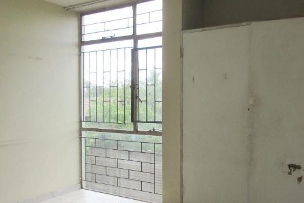 An empty bedroom featuring a built-in wardrobe, tiled flooring, and large windows fitted with security bars.