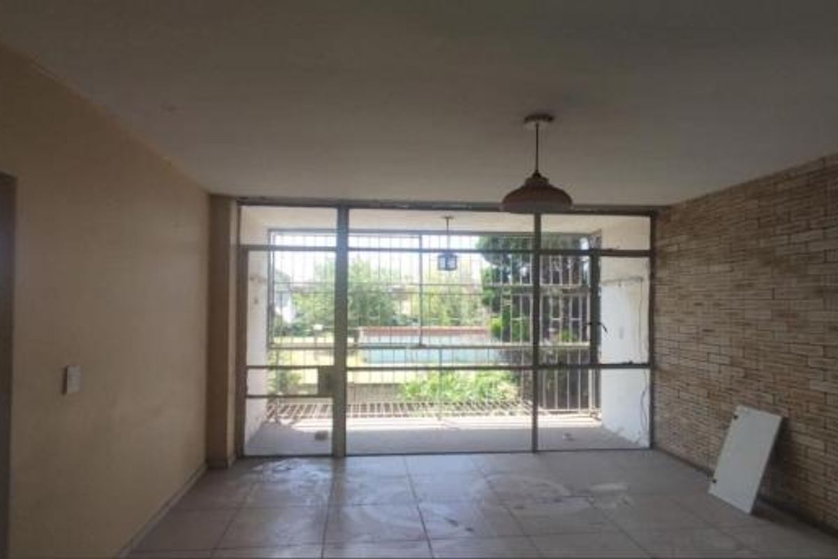 Spacious living area featuring a brick accent wall, tiled flooring, and large glass doors leading to an outdoor balcony area.