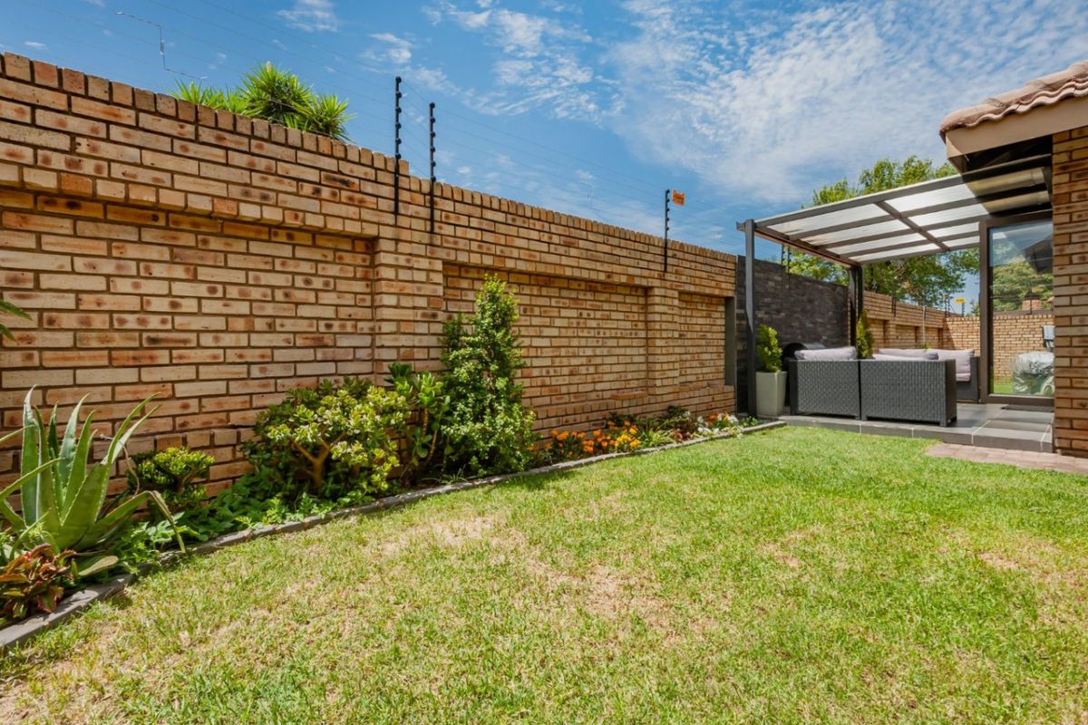 A well-maintained rear garden featuring a face brick boundary wall with electric fencing and a covered patio area with tiled flooring.