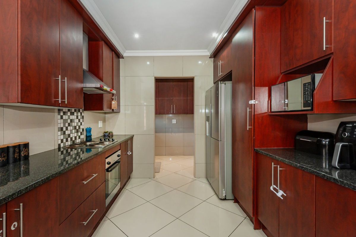 A well-maintained galley-style kitchen featuring dark wood cabinetry, granite countertops, built-in oven, gas hob, and a convenient adjoining scullery area.