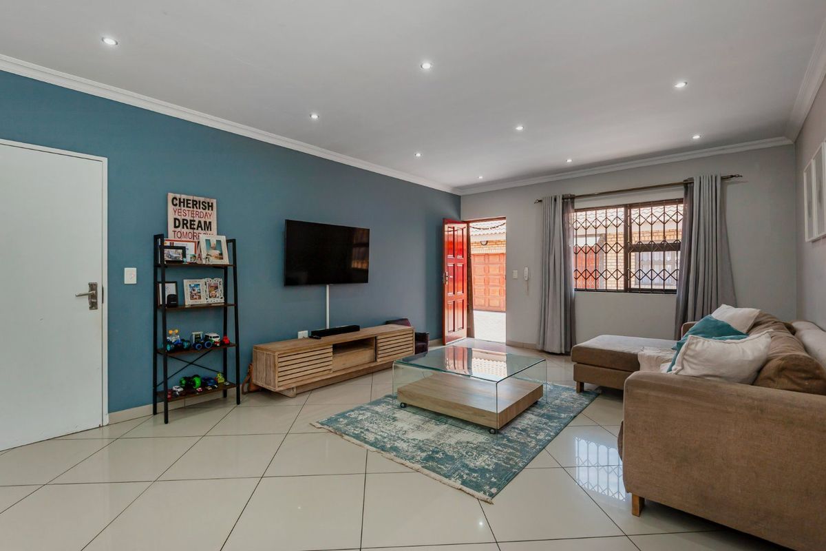 A well-maintained living room featuring tiled flooring, recessed downlighting, and a feature wall, with direct access to the exterior.