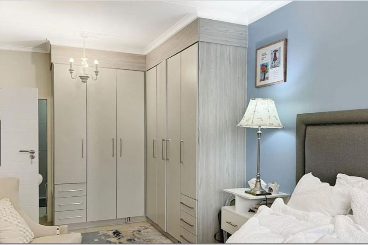 A well-maintained bedroom featuring extensive floor-to-ceiling built-in cupboards with modern wood-grain finish and decorative coving.