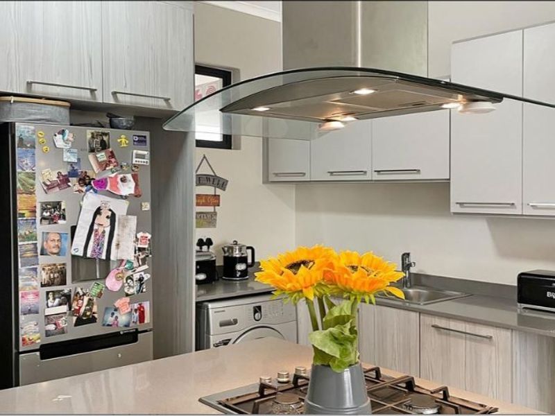 Modern kitchen featuring light wood-grain cabinetry, stone countertops, a central island with a gas hob, and a sleek glass extractor fan.