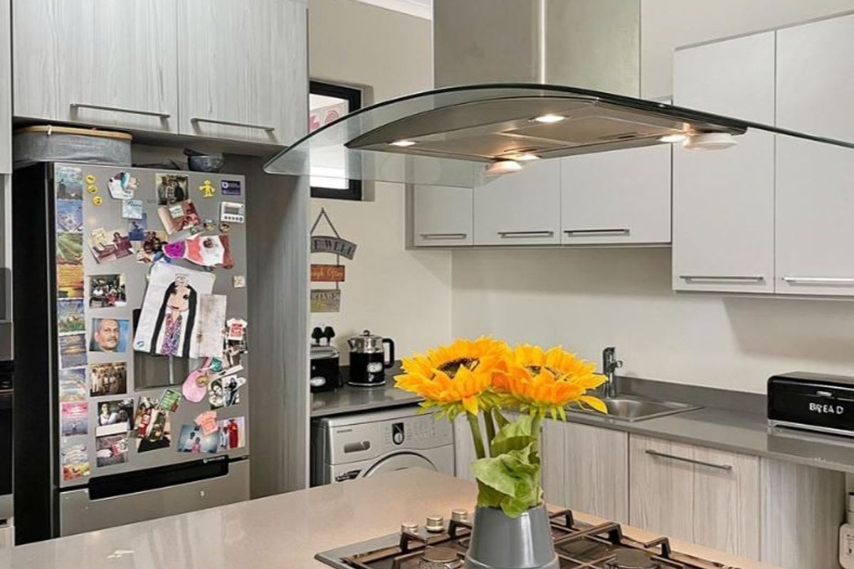 Modern kitchen featuring light wood-grain cabinetry, stone countertops, a central island with a gas hob, and a sleek glass extractor fan.