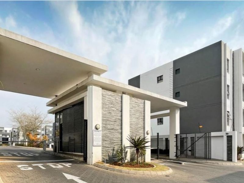 Modern apartment complex entrance featuring a secure gatehouse, boom gate access, and contemporary architectural design with stone cladding and concrete finishes.