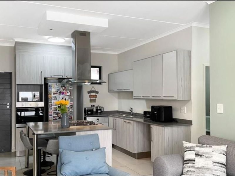 Modern open-plan kitchen featuring light wood-grain cabinetry, stone countertops, built-in oven, gas hob, and a stainless steel extractor fan, seamlessly integrated with the living area.