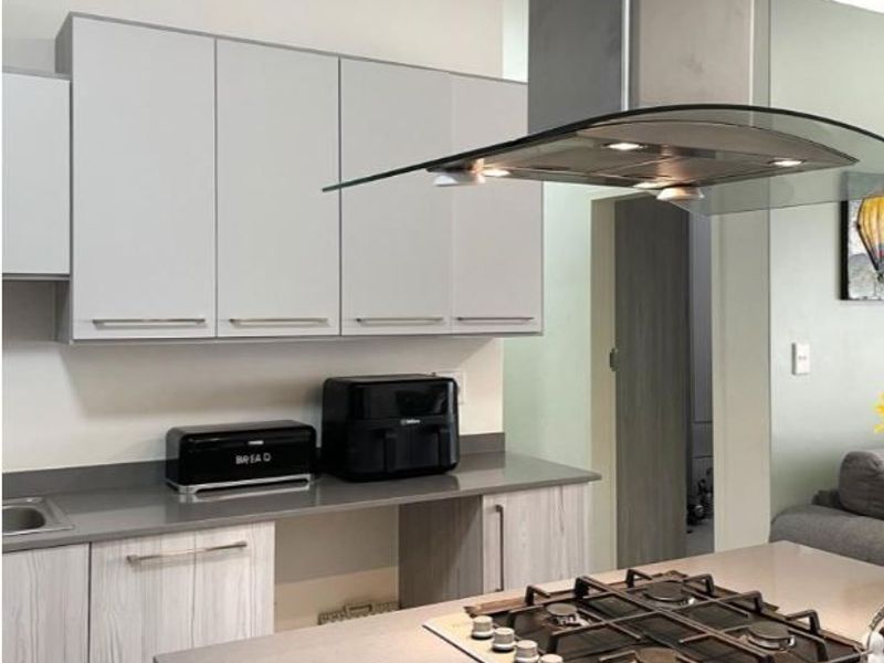 Modern kitchen featuring light grey cabinetry, stone countertops, a gas hob with a glass extractor hood, and clean, contemporary finishes.