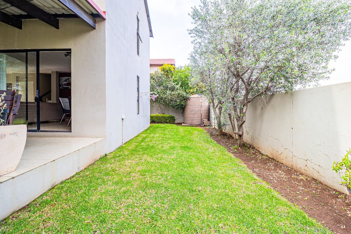 A rear garden view featuring a lawn, a water storage tank, a boundary wall, and a covered patio area with sliding door access.