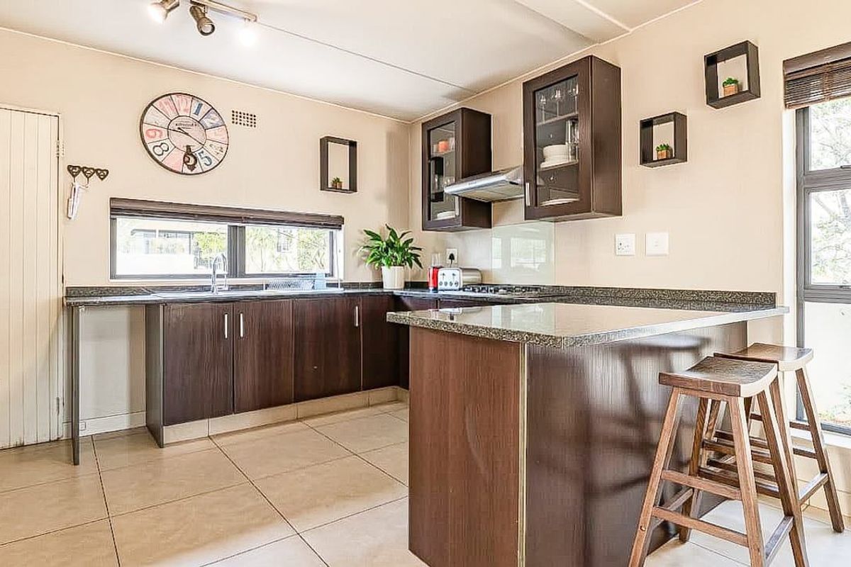 A functional kitchen featuring dark wood cabinetry, granite countertops, a breakfast bar, and tiled flooring with ample natural light.