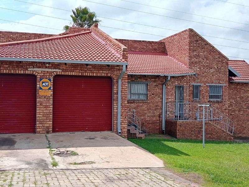 A face-brick residential house featuring a double garage with red roller doors, tiled roof, and a paved driveway entrance.