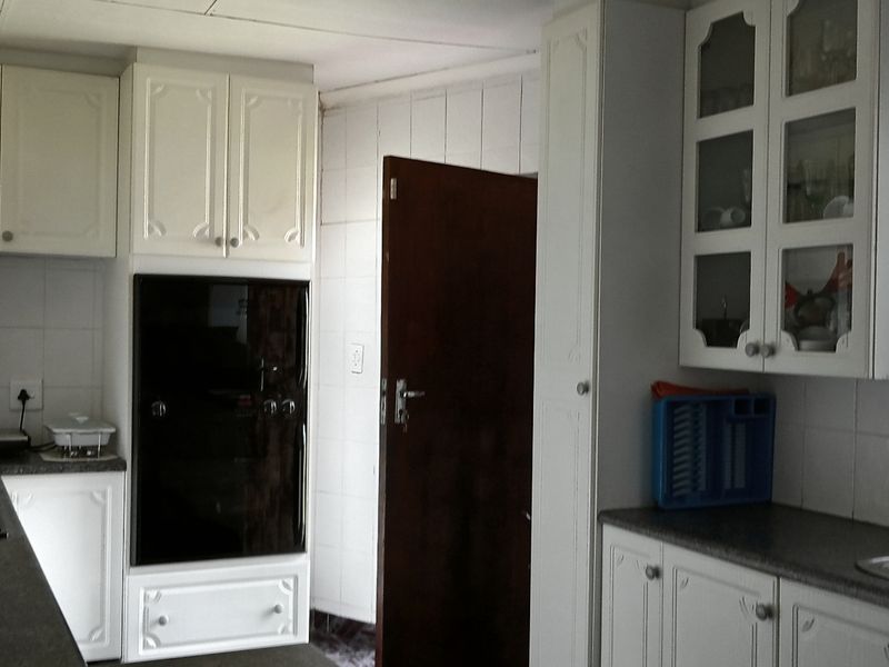 A functional kitchen featuring white cabinetry, built-in oven, hob, and tiled splashbacks with a stainless steel sink.