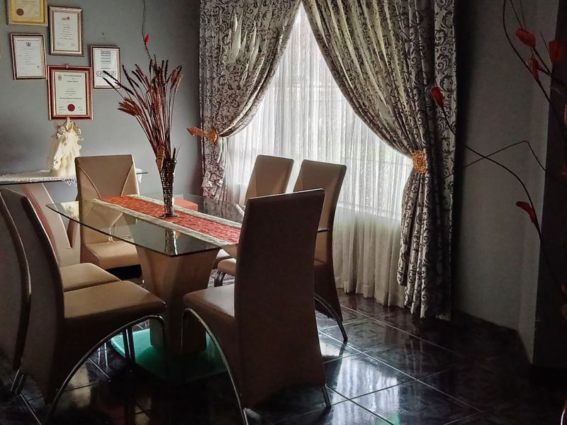 A formal dining room featuring dark tiled flooring and large windows with decorative curtains, providing a dedicated space for family meals and entertaining.