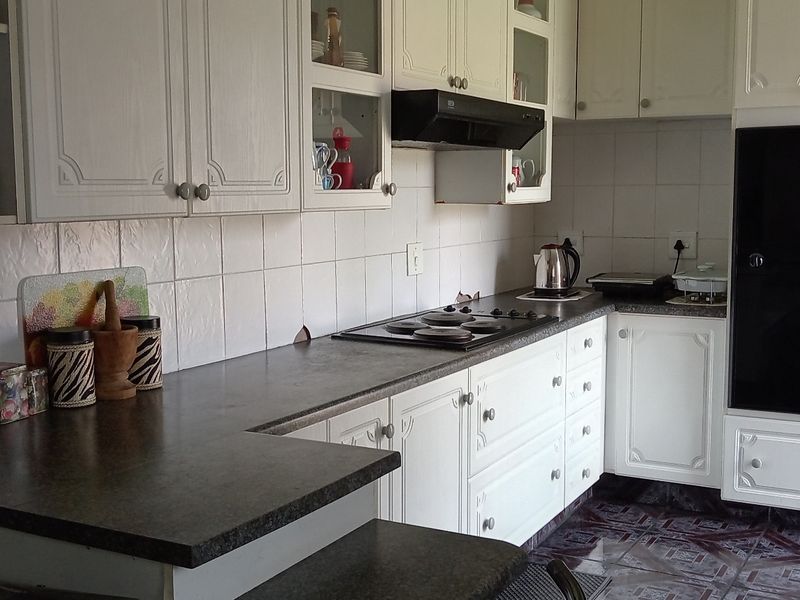 A functional kitchen featuring white cabinetry, dark countertops, a built-in oven, and a hob with an extractor fan.