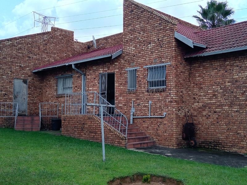 Rear view of a face-brick house featuring a raised patio area, metal security gates, and a spacious garden with a lawn.