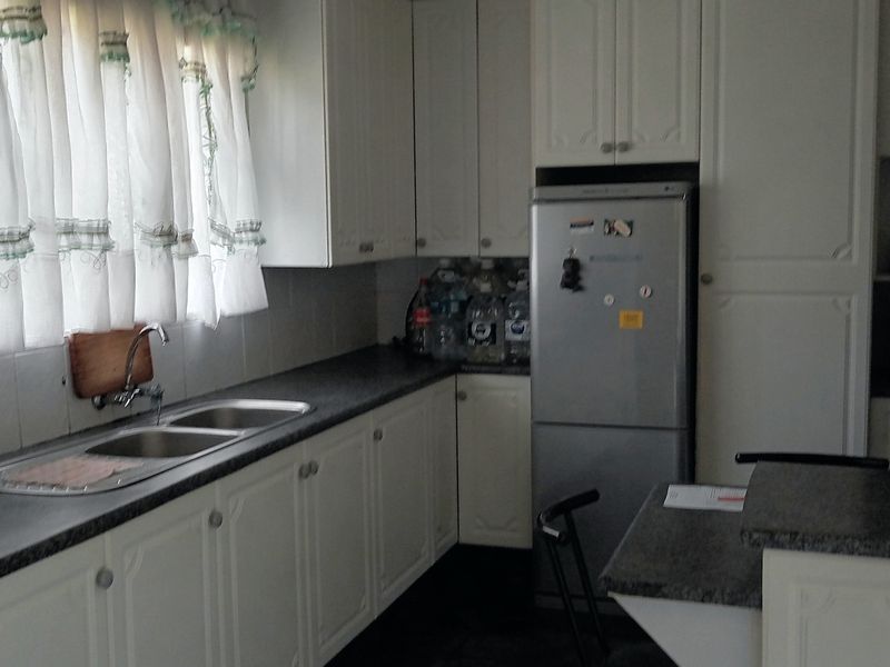 A functional kitchen featuring white cabinetry, dark laminate countertops, a double-basin stainless steel sink, and dedicated space for a refrigerator.