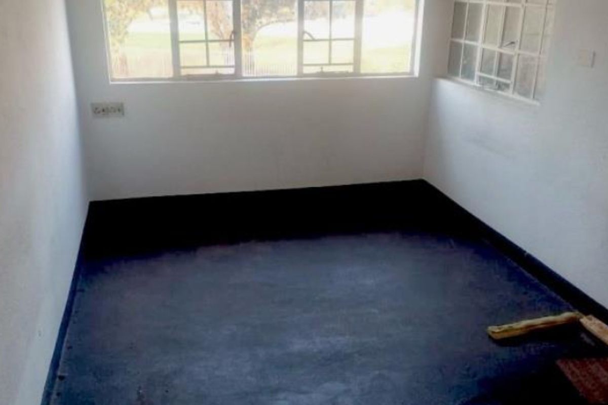 An empty bedroom featuring multi-pane windows and basic electrical fixtures, requiring flooring and wall finish updates to improve its overall condition.