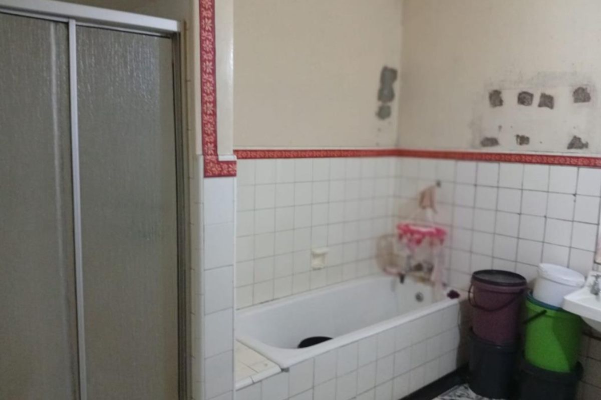A dated bathroom featuring a built-in bathtub and shower enclosure, currently requiring significant cosmetic repairs and wall surface restoration.