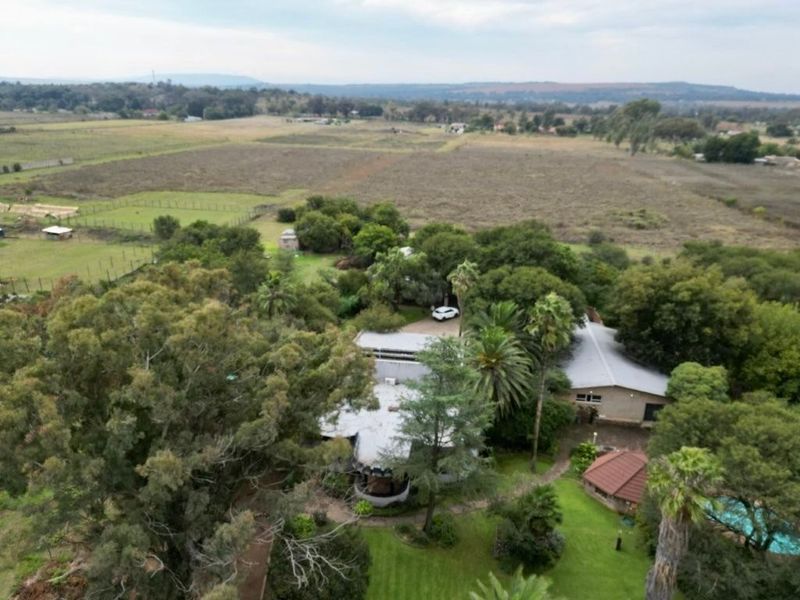 Aerial view of a large residential property featuring extensive landscaped gardens, mature trees, and a swimming pool set within a rural landscape.