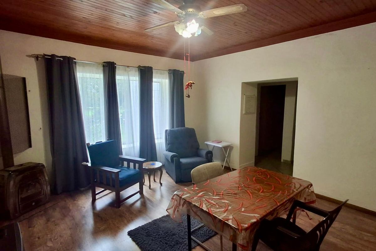 Living area featuring a wood-burning fireplace, timber-clad ceiling, and large windows providing natural light.
