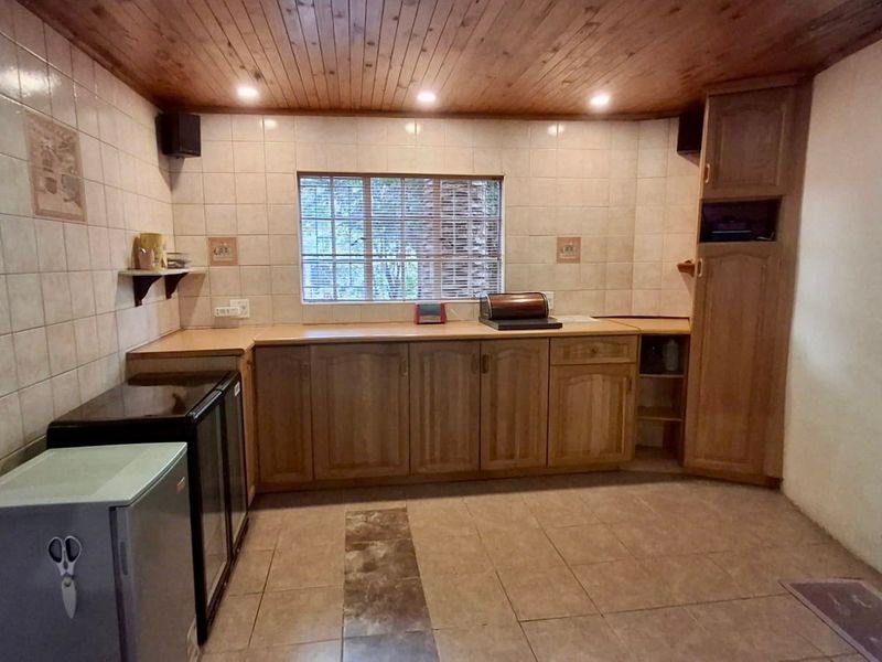 A functional kitchen featuring timber cabinetry, tiled splashbacks, a timber-paneled ceiling, and tiled flooring with a central decorative inlay.